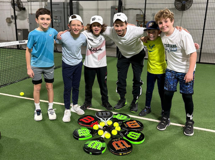 Group of young boys gathered around an array of padel equipment