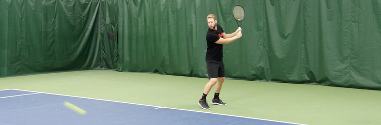 Tennis instructor on court in two-handed backhand stance.
