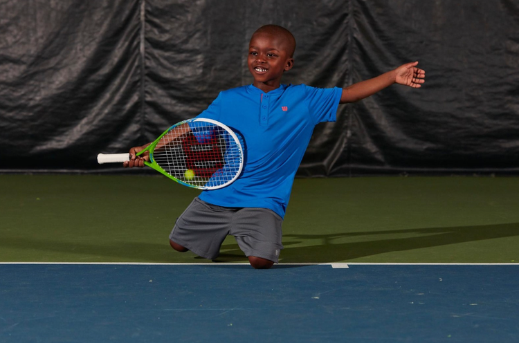 Young boy backhanding a tennis ball on the court