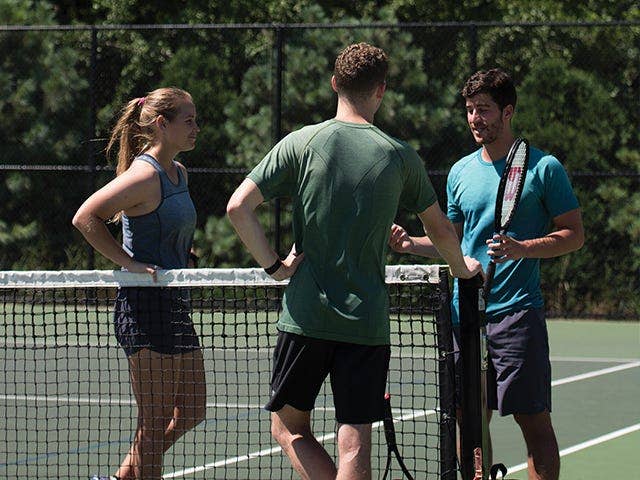 three players talking on a tennis court